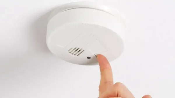 person pressing test button on smoke alarm